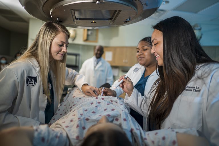 Three students examine a patient under a radiation machine while a teacher looks on in the back