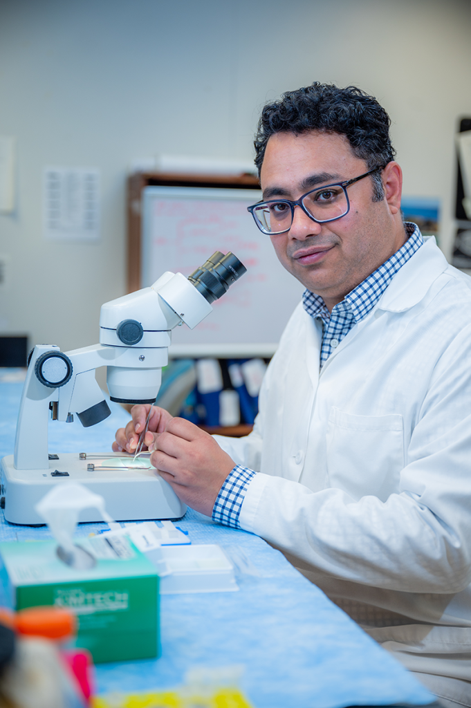 man in white lab coat uses a microscope in a lab