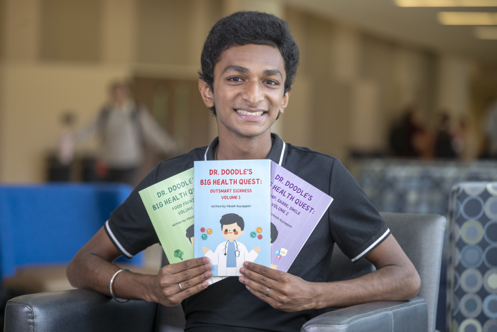 Student holds three books he wrote