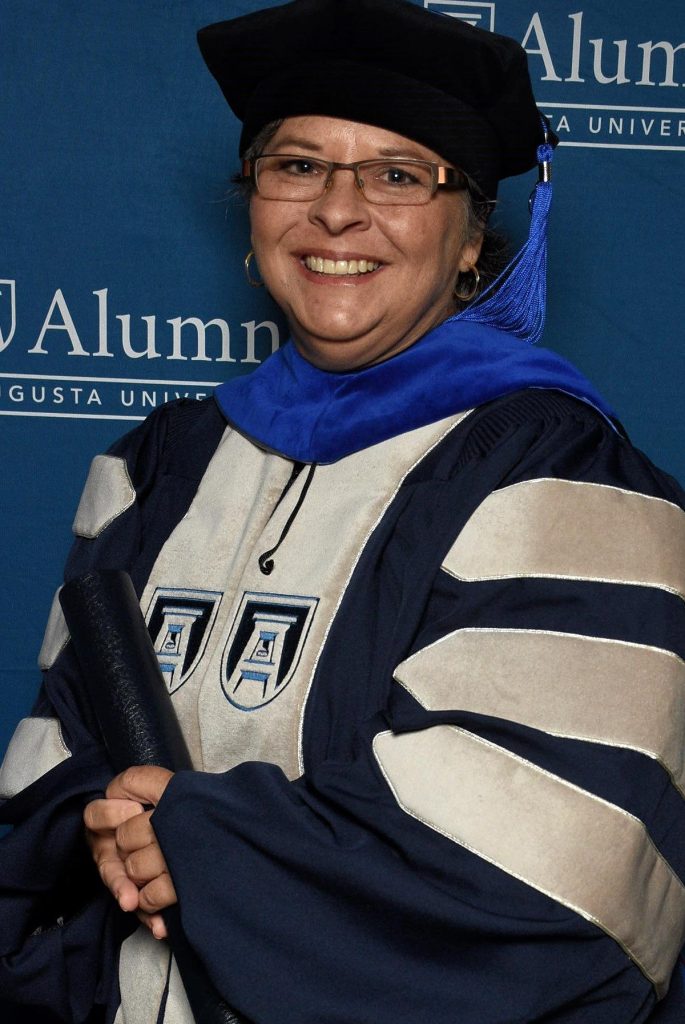 woman in her graduation cap and gown with a diploma in hand