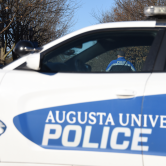 Augusta University police officer stands behind a police cruiser