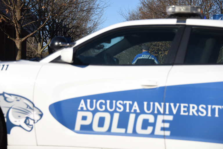 Augusta University police officer stands behind a police cruiser