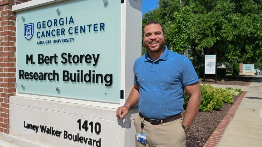 Man in a blue polo shirt stands beside the M. Bert Storey Research Building sign