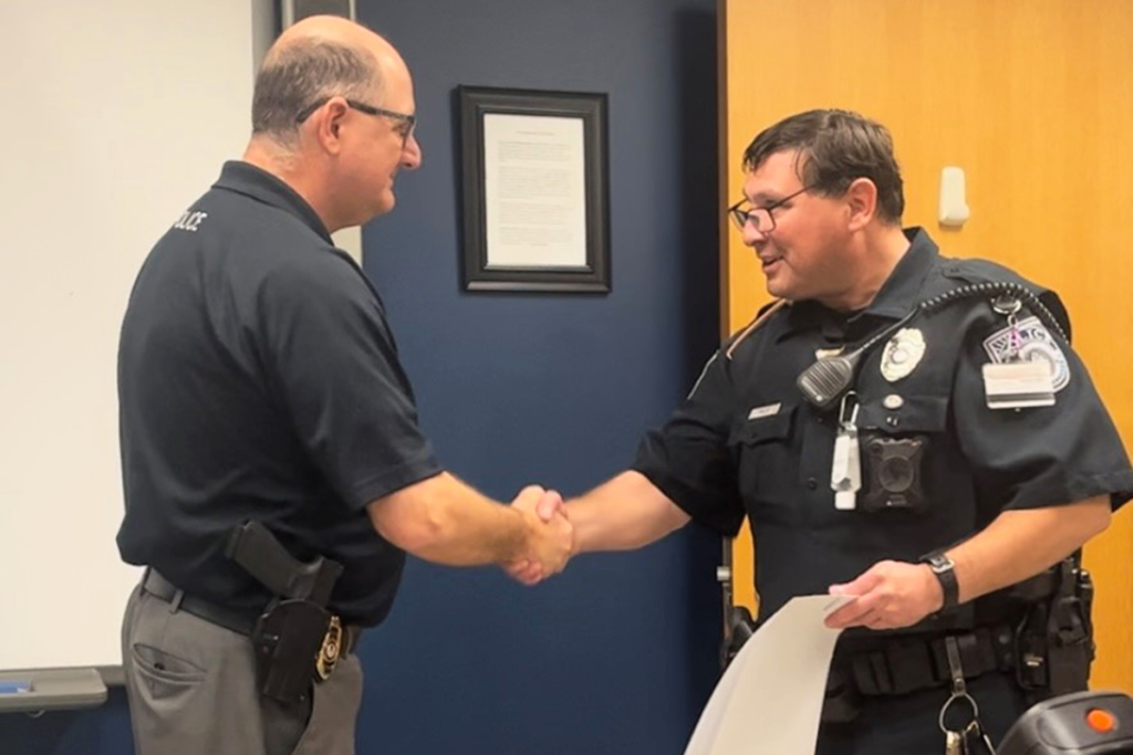 A man hands a male police officer a certificate and shakes his hand