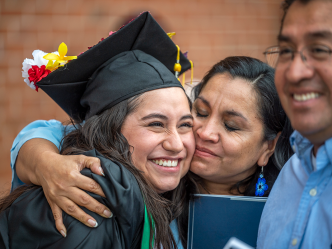 A woman hugs her daughter who is wearing a graduation cap and gown.