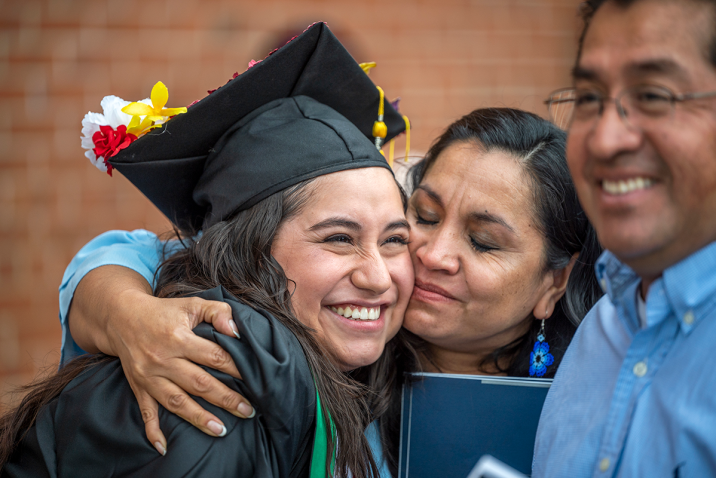 A woman hugs her daughter who is wearing a graduation cap and gown.