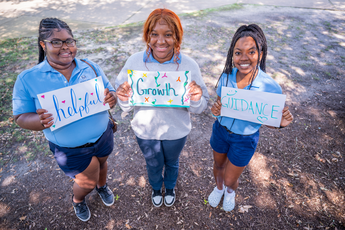 Three female Orientation Leaders at Augusta University holding hand-made signs that read "helpful","growth", and "guidance."