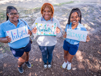 Three female Orientation Leaders at Augusta University holding hand-made signs that read "helpful","growth", and "guidance."