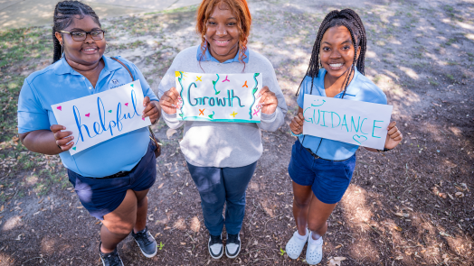 Three female Orientation Leaders at Augusta University holding hand-made signs that read "helpful","growth", and "guidance."