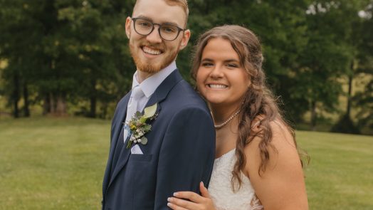 a bride stands behind her husband as they smile at the camera on their wedding day