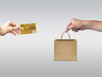 a computer with a hand holding a credit card coming out of it faces a computer with a hand holding a shopping bag coming out of it