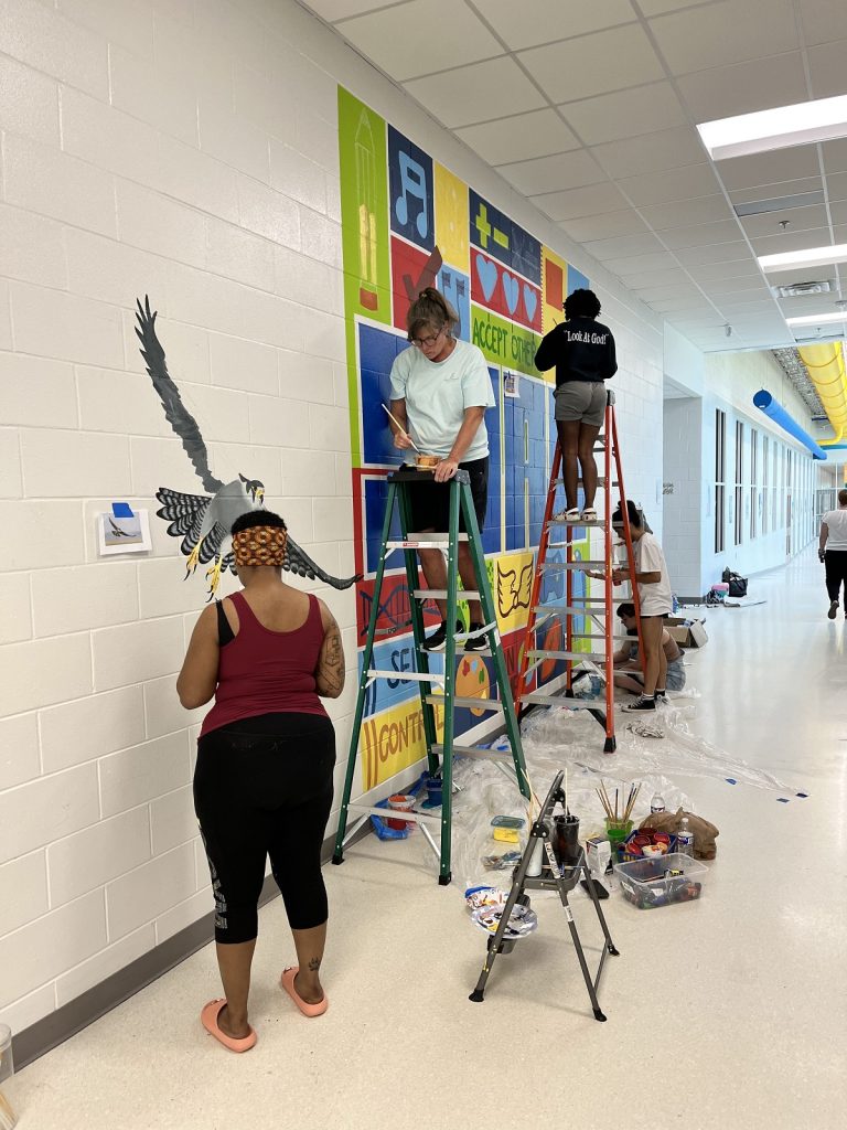 students on ladders painting a mural