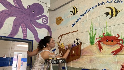 student painting a mural of an underwater landscape