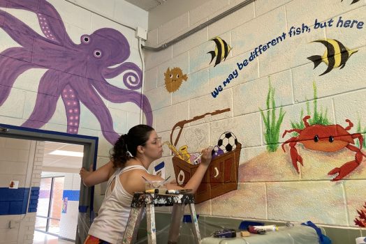 student painting a mural of an underwater landscape