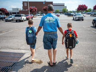 Adult walking with two kids wearing backpacks