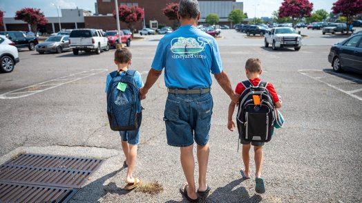 Adult walking with two kids wearing backpacks