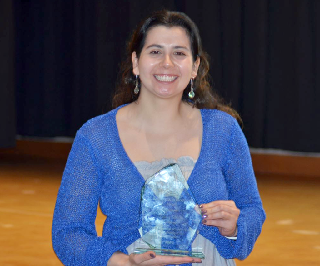 A woman holds an award and smiles for a photo.