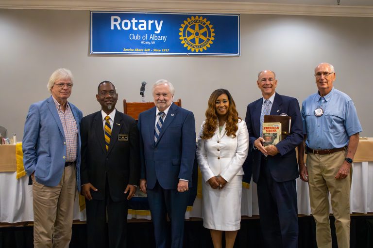 A group of people, including five men and one woman, stand in front of a podium and pose for a photo.