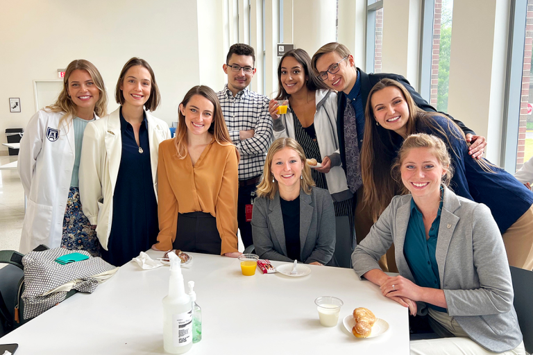 A group of college students sit at a table and smile for a photo.