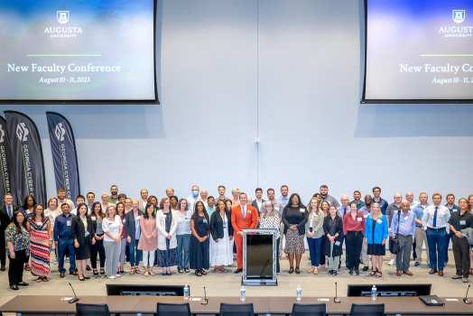 80 people pose for group photo on stage.