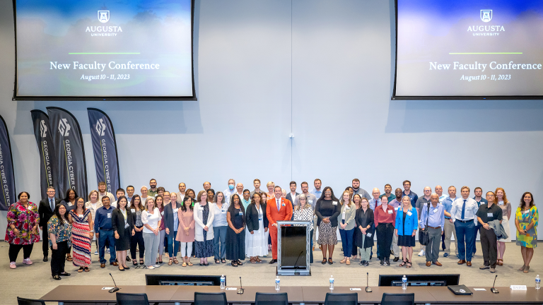 80 people pose for group photo on stage.