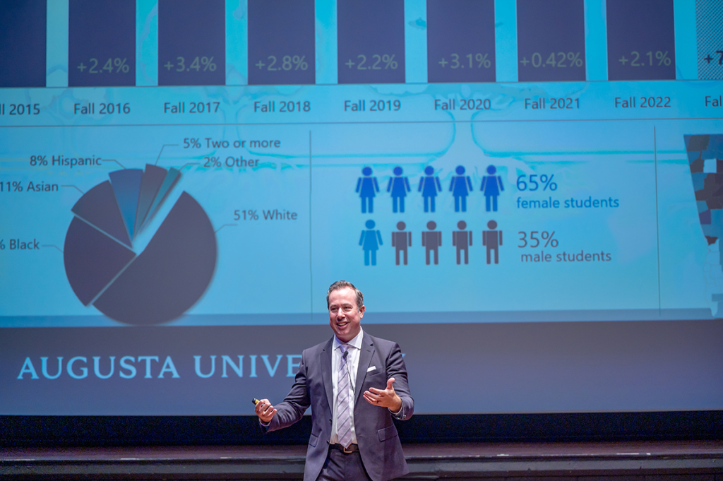 Man in a suit presents a slide with statistics to a group of people.