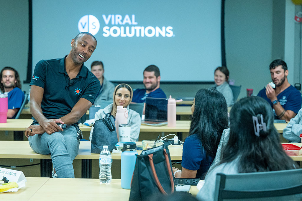 A man sits on a table, while talking to students