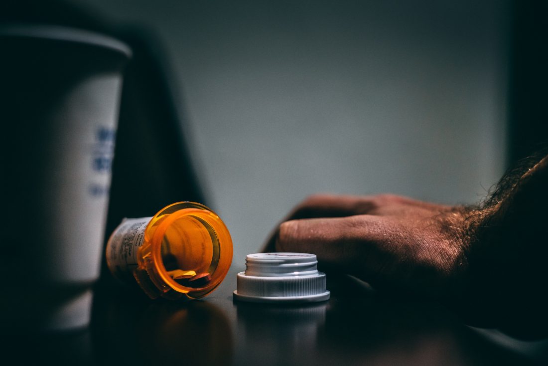 open bottle of pills, coffee cup and person's hand on a table
