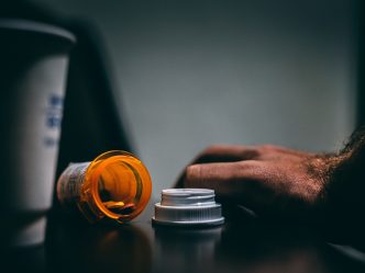 open bottle of pills, coffee cup and person's hand on a table