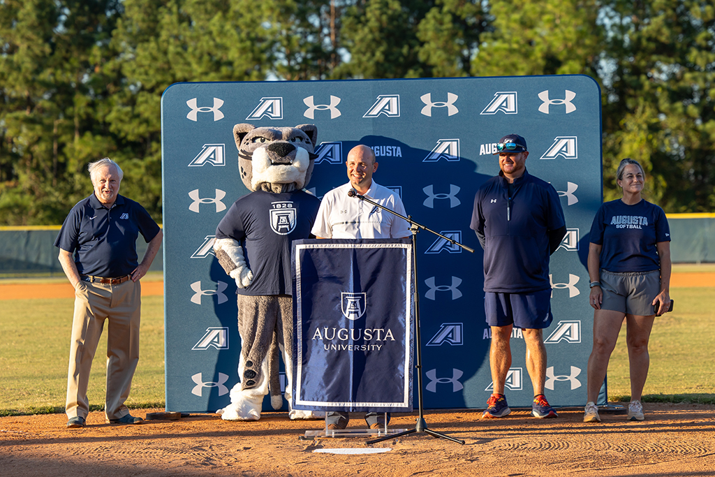 Three men, a woman and a mascot standing behind a podium