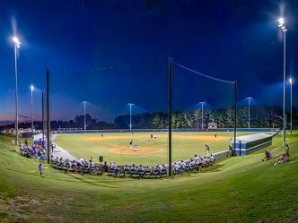 People sitting around a baseball field with lights on