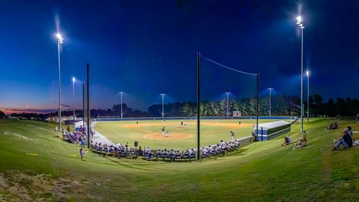 People sitting around a baseball field with lights on