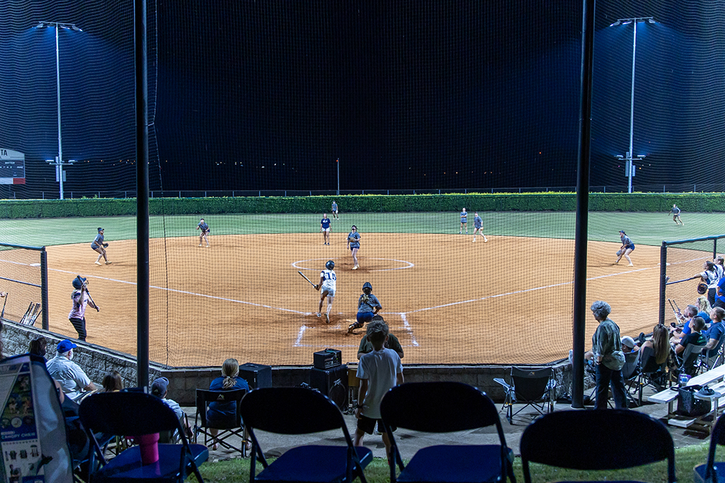 People sitting around a softball field under the lights