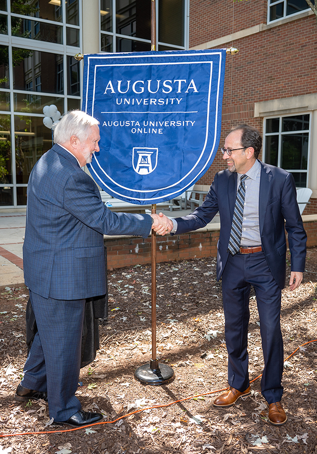 Two men wearing suits shake hands outside.