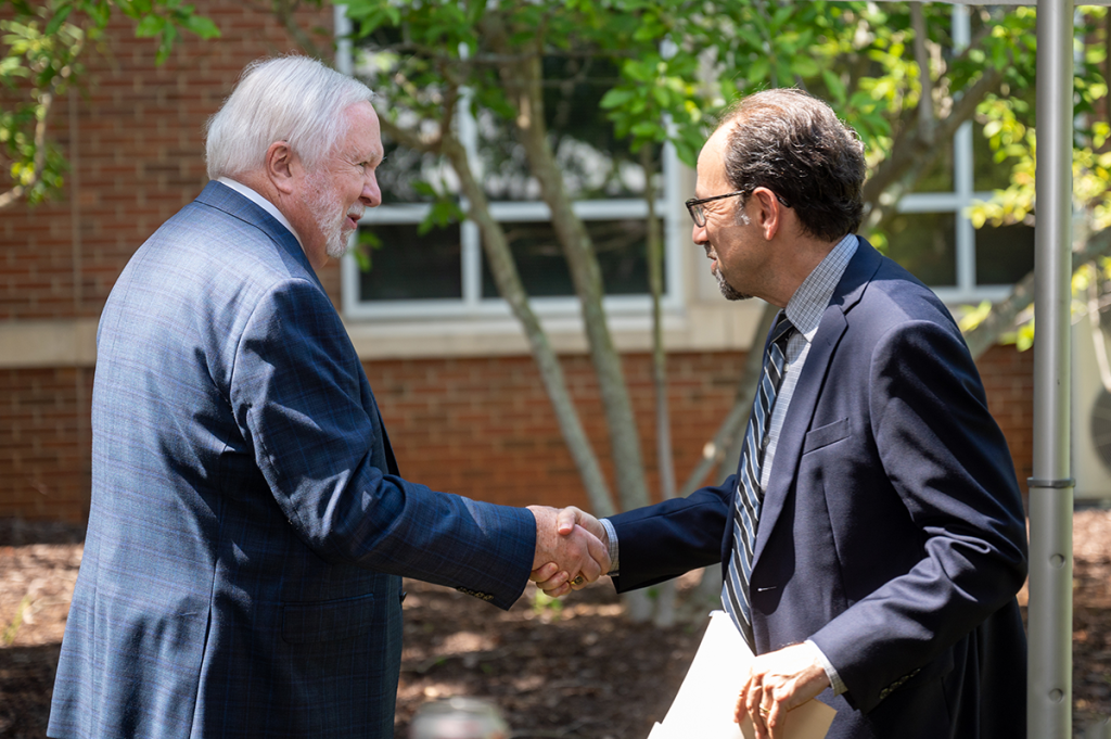 Two men in suits shake hands outside.