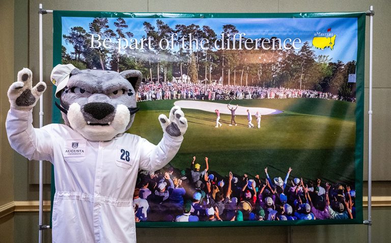 Augustus standing in front of a banner from Augusta National