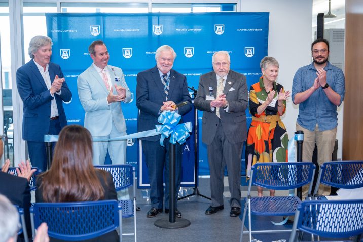 Deans, the Au President, the AU Provost, an AU Foundation member and a graduate student stand behind a ribbon as it is cut.