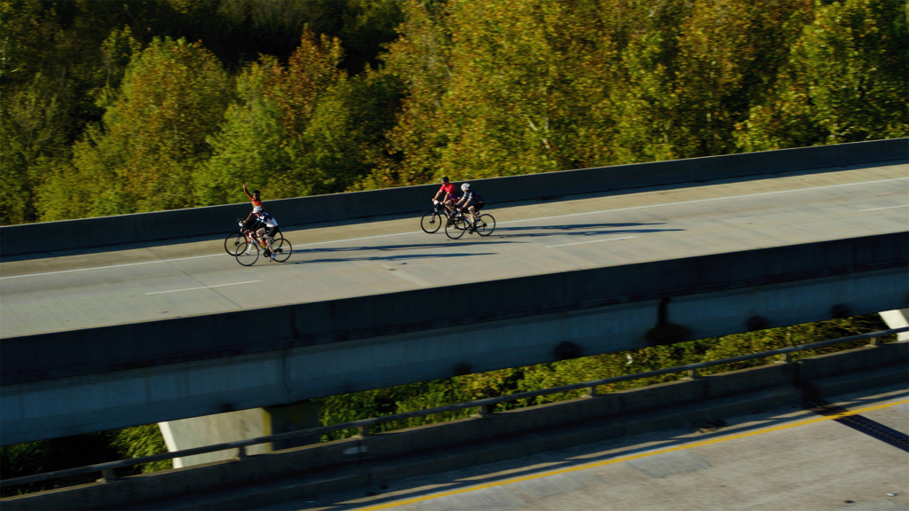 Bikers ride along bridge.