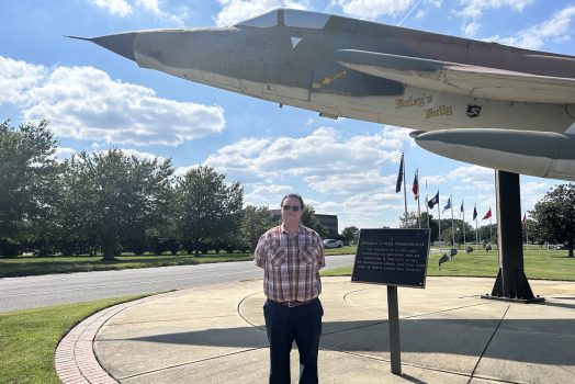 Man poses for a photo under a mounted plane
