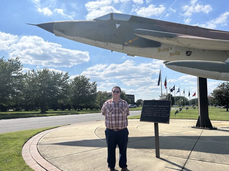 Man poses for a photo under a mounted plane