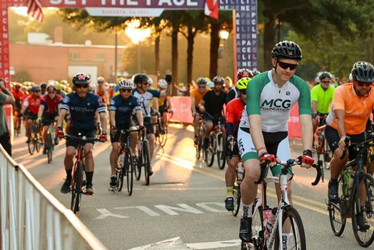 riders pass under a Set the Pace banner