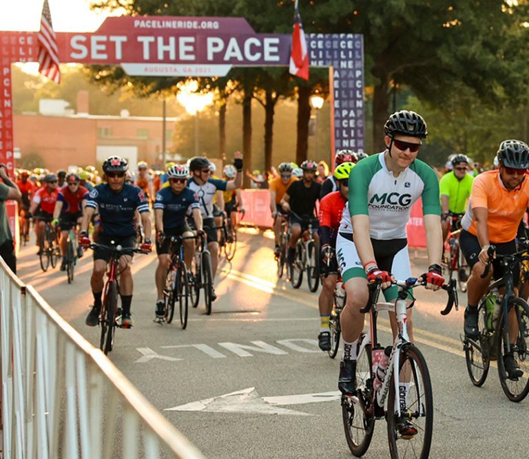 riders pass under a Set the Pace banner