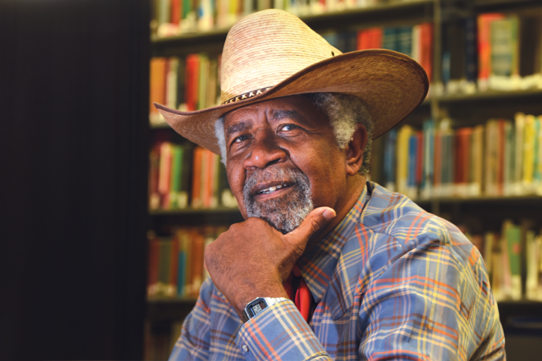 A man in a cowboy hat sits in front of rows of books
