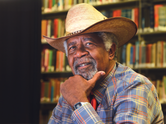 A man in a cowboy hat sits in front of rows of books