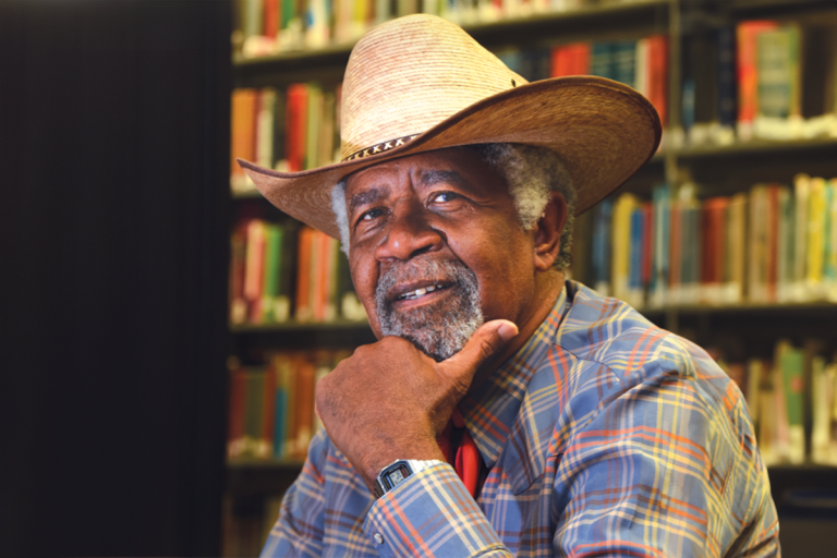 A man in a cowboy hat sits in front of rows of books