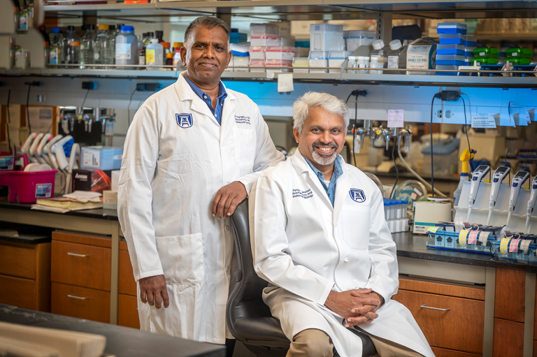 Two men wearing lab coats pose for a photo in a science lab.