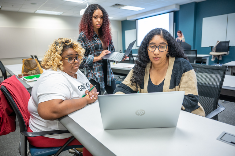 An Augusta University professor talking to two psychology students inside a classroom.