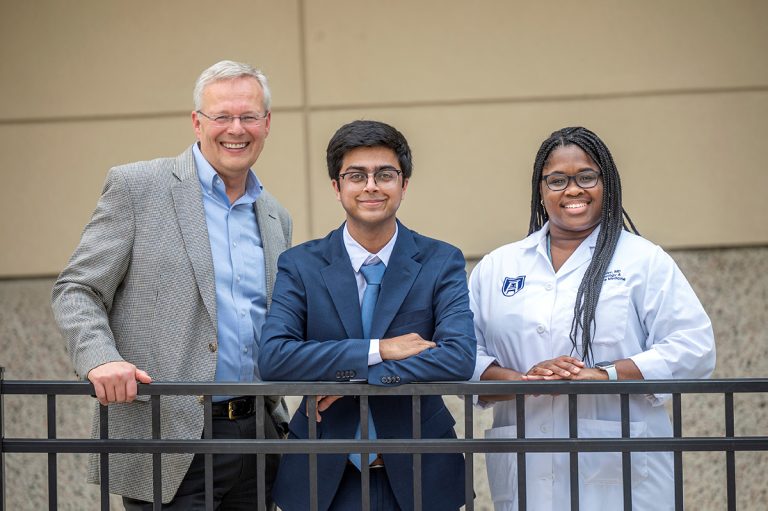 Three people stand in front of railing smiling