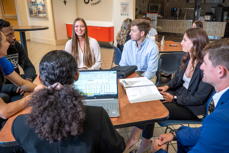 Students from Augusta University's Hull College of Business sit at a table having a conversation.