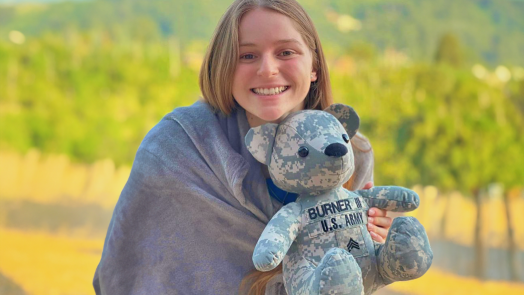 a young woman holds a stuffed Teddy bear with the words "Burner III U.S. Army" on it